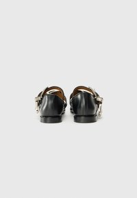 Black leather shoes with a low heel, back buckle detail, and an open back design. Smooth texture with minimalistic accents.