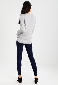 Lysegrå langærmet skjorte parret med mørkeblå skinny jeans og sorte/sandaler med åbne tæer. Glat stof finish og afslappet pasform.