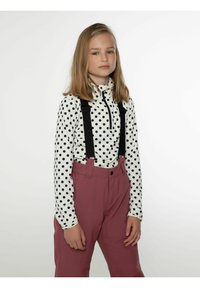 Pitkähihaine pilkkupaita valkoisena ja mustana, jossa on vetoketju-herra, yhdistettynä vaaleanpunaisiin korkeavyötäröisiin housuihin, joissa on mustat henkselit.