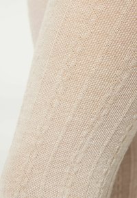 Beżowe rajstopy dziane z teksturowanym wzorem, z wypukłymi liniami i diamentowymi kształtami, wykonane z miękkiego, oddychającego materiału.