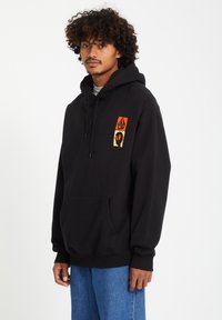 Zwarte hoodie met een voorzak, trekkoord capuchon, met een oranje en gele grafische afbeelding op de linkerkant van de borst. Gemaakt van katoen.