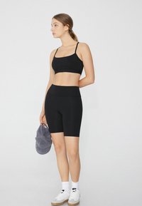Conjunto de sujetador deportivo negro y shorts, fabricado con una tela suave, con tirantes delgados, cinturilla alta y silueta ajustada. Se sostiene una gorra gris.