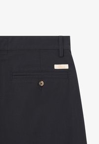 Pantaloni blu navy con frontale piatto, caratterizzati da una tasca posteriore con chiusura a bottone e un piccolo etichetta in tessuto beige cucita sulla vita.