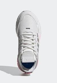 Białe buty sportowe z teksturowanym wierzchem, szarymi paskami akcentującymi, wyściółką na języku i różową podeszwą. Posiadają tradycyjne sznurowanie oraz oznakowaną zakładkę na pięcie.