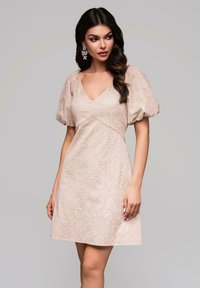 Robe à manches courtes, décolleté en V en tissu beige clair texturé avec des motifs en tourbillon. Longueur au-dessus du genou, corsage ajusté, jupe évasée.
