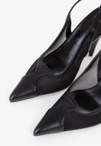 Zapatos de tacón alto negros tipo slingback con puntera afilada, detalles de malla en los lados y un acabado en cuero suave alrededor de la puntera.