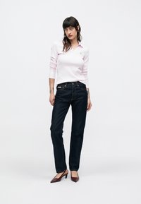 Polo a maniche lunghe color rosa chiaro con colletto, abbinata a jeans blu scuro a gamba dritta e scarpe con tacco color marrone scuro.