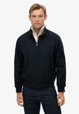 Navy blue, lightweight bomber jacket with a zip front, snap collar, ribbed cuffs, and side pockets. Features subtle logo detail on chest.