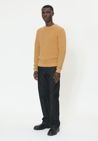 Pull en maille couleur moutarde avec col rond, associé à un jean droit bleu foncé et des chaussures en cuir noir. Design simple et texturé.