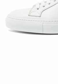 Baskets blanches avec une tige en cuir lisse, bout arrondi et semelle en caoutchouc ; elles sont dotées d'un système de laçage et de détails texturés sur le bord de la semelle.