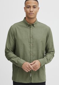 Olive green long-sleeve shirt with a button-down collar, featuring brown buttons and a subtle texture. Front placket and cuffs visible.