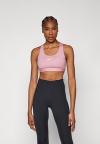 Rožinė sportinė liemenėlė su plačiu dirželiu ir baltu Nike logotipu, derinama su aukšto liemens juodomis legging'ais. Lygi audinio tekstūra, sportinis dizainas.