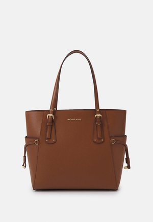 Brązowa skórzana torba typu tote z podwójnymi uchwytami, bocznymi detalami z klamrami oraz małym złotym logo „Michael Kors” na środku z przodu.
