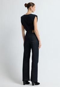 Černý top bez rukávů se strukturovanými ramenními částmi v kombinaci s kalhotami s vysokým pasem v tmavém denimu a širokém střihu. Hladká textura, viditelný detail šití.