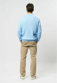 Lichtblauwe kabelgebreide trui met lange mouwen, gecombineerd met khaki rechte broek en witte schoenen met gekleurde accenten.