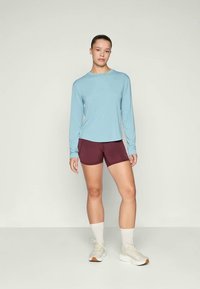 Top de manga longa azul claro, calções bordeaux, ténis creme, meias brancas. Tecido suave, design atlético casual, corte descontraído, acentos mínimos.