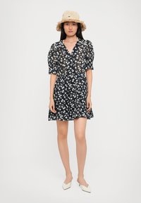 Rochie cu mânecă scurtă, de culoare bleumarin, cu un model floral alb, talie strânsă și fustă evazată. Asortată cu o pălărie din paie și pantofi albi cu vârful ascuțit.