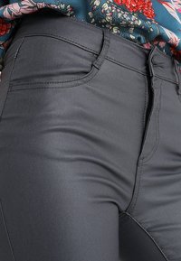 Pantalones ajustados gris oscuro hechos de tela suave, con cremallera frontal, costuras visibles y dos bolsillos frontales.