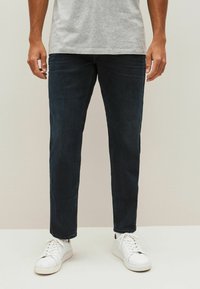 Donkerblauwe spijkerbroek met een recht model, gecombineerd met witte sneakers. De stof heeft een klassieke textuur en minimale details.