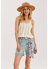 Pletený top na ramienka v krémovej farbe s výstrihom do V a textúrovaným vzorom, spárovaný s svetlomodrými denimovými šortkami a šatkou s kvetinovým motívom zviazanou okolo pása.