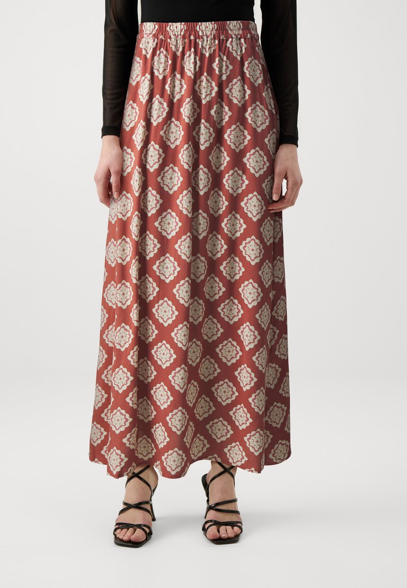 Gonna maxi in ruggine con motivo floreale crema, cintura elastica arricciata, design fluido, abbinata a sandali neri con cinturini.