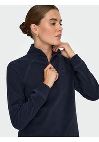 Tamno plavi flis pulover s polu-zip ovratnikom, koji ima logo planine na prsima i teksturiranu tkaninu za toplinu.