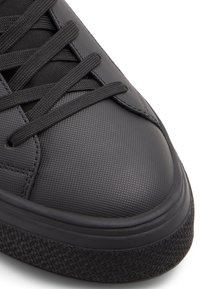 Zapatilla negra con parte superior texturizada, con cordones planos, puntera redondeada y suela de goma con un dibujo para mayor agarre.