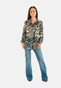 Langarm, knoop-overhemd met een leopardprint in tinten beige, zwart en teal, gecombineerd met uitlopende blauwe jeans.