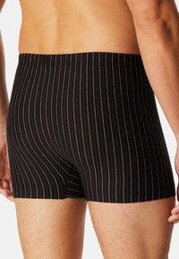 Boxers à rayures noires avec des rayures verticales rouges et blanches. Tissu doux avec une taille élastique, coupés à mi-thigh.