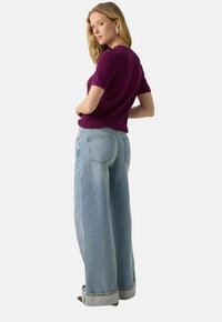 Paarse gebreide trui met korte mouwen, gecombineerd met lichtblauwe brede jeans met opgerolde zoom en een vijf-pocket ontwerp.