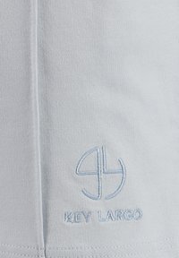 Himmelblaues Baumwollgewebe mit einem gestickten Logo, das die Buchstaben "KL" und den Text "KEY LARGO" in blassblauer Farbe am unteren Rand zeigt.