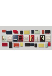 Quaderni Moleskine di vari colori tra cui rosso, blu, nero, verde e giallo, disposti per formare la parola "MOLESKINE." Copertine texture e fasce elastiche visibili.