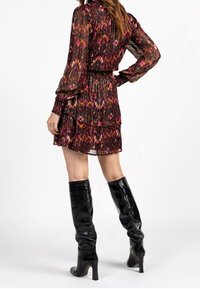 Vestido mini de color negro y con estampado multicolor, de mangas largas, textura plisada y cintura ajustada, combinado con botas negras brillantes hasta la rodilla.