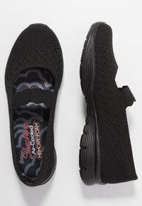 Czarne buty Skechers wykonane z oddychającego materiału dzianinowego, z wyściełaną wkładką z pianki Air-Cooled Memory Foam i elastyczną podeszwą. Posiada pasek dla pewnego dopasowania.