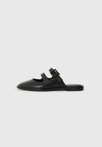 Black slip-on shoe made of glossy material, featuring cut-out design and adjustable strap with hardware accent. Flat sole with minimal tread.