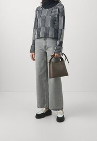 Maglione corto a righe bianche e nere, jeans a gamba larga grigio chiaro, scarpe bianche e nere e una piccola borsa marrone con manico circolare.