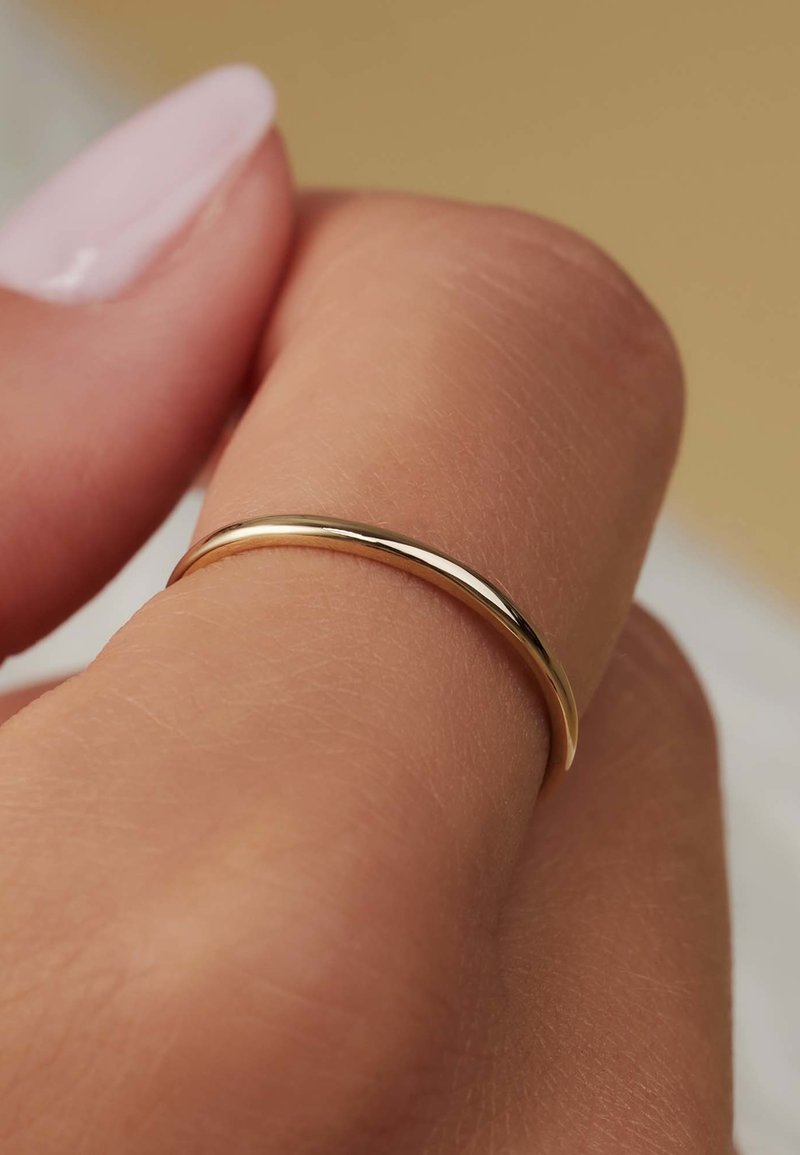 Bague en or avec un anneau lisse et arrondi, présentée sur le bout d'un doigt. Caractérisée par une surface polie et une courbure subtile.