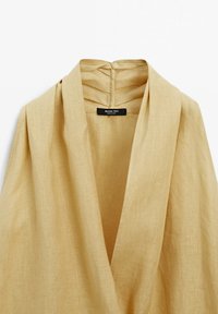 Linneblus i ljus beige med draperad halsringning och en subtil struktur. Etikett på baksidan med texten "Massimo Dutti." Slät tygfinish.