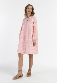 Rúžovým vzorovaným šatám s dlhými rukávmi, okrúhlym výstrihom a zhrnutou tiered sukňou dopĺňajú sandále s kríženými popruhmi.