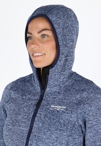 Felpa con zip di colore blu navy in tessuto texturizzato, fodera interna nera a contrasto e colletto alto. Presenta un logo sul petto.