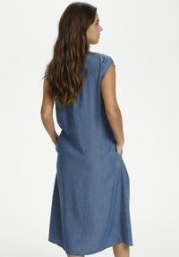 Abito midi in denim blu con maniche corte, tasche laterali e vestibilità rilassata. Tessuto liscio e leggera forma a campana nell'orlo.