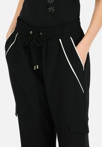 Pantalons de jogging noirs avec une taille élastique, fermeture à cordon de serrage, rayures blanches sur les côtés et poches latérales. Fabriqués en matériau doux et confortable.