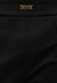 Μαύρο ύφασμα με κεντρική ραφή και μαύρο φιόγκο με χρυσή ετικέτα λογότυπου «Versace Jeans Couture».