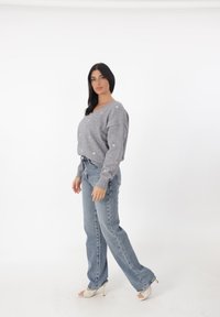 Maglione grigio con accenti a forma di cuore dorati, design a scollo a V, abbinato a jeans azzurri chiari e sandali con tacco bianchi. Tessuto morbido e vestibilità rilassata.