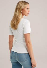 Weißes, geripptes T-Shirt mit kurzen Ärmeln, taillierte Passform und glatter Textur, getragen mit blauen Jeans.