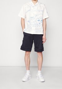 Krótki rękaw, biały koszulka z niebieskimi graficznymi rysunkami; połączona z granatowymi szortami z miękkiego materiału; białe sneakersy dopełniają wygląd.