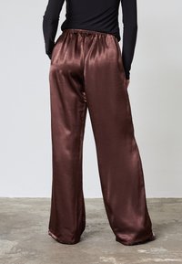 Brune satin brede bukser med elastisk talje, der har en glat tekstur og flydende design. Skræddersyet til en afslappet pasform.