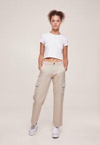 Lyse beige cargo-bukser med sidelommer, med en avslappet passform. Kombinert med en hvit kortermet t-skjorte og hvite sneakers.