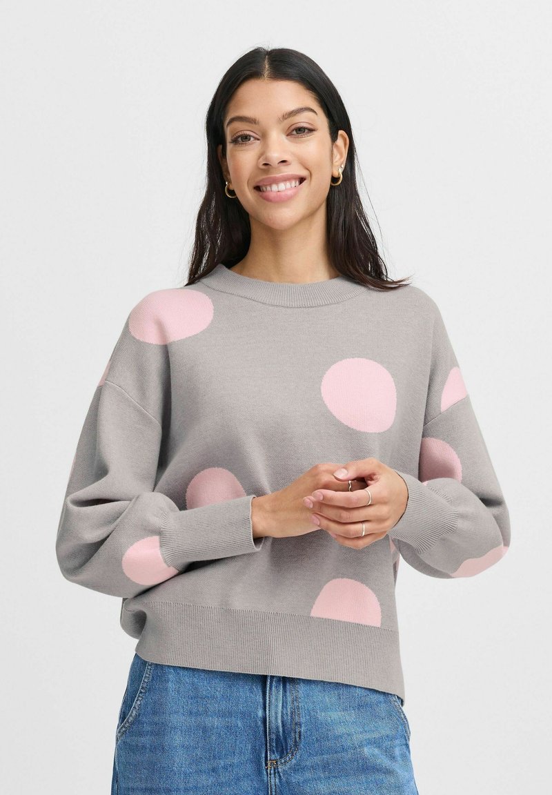 Gray sweater featuring large pink polka dots, ribbed cuffs and hem, boxy fit, and textured knit material. Worn with blue jeans.