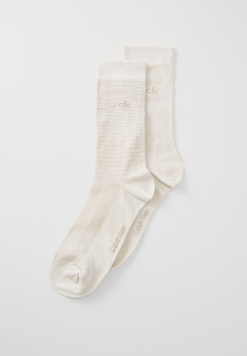 Calcetines de mezcla de algodón blancos con un patrón texturizado, puños acanalados y una marca en relieve "ck" y "Calvin Klein" cerca del tobillo.